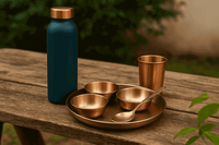 Set of brass kitchen utensils including bowls, a spoon, and a cup on a wooden table with a blue bottle in the background.
