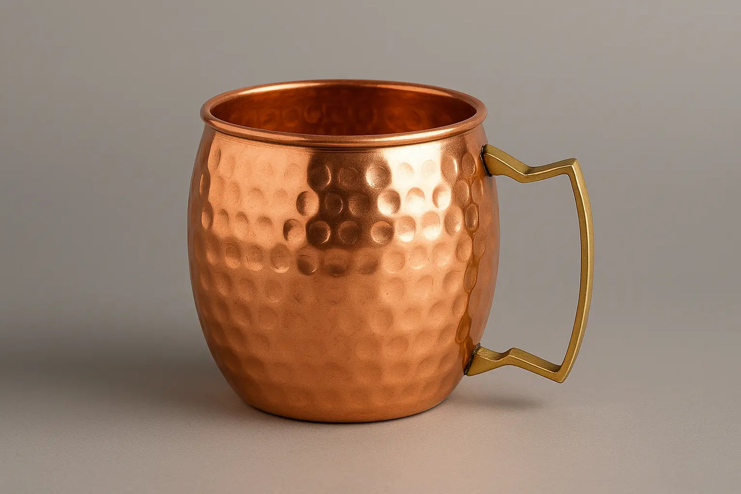 Copper mug with a textured surface and gold handle on a gray background
