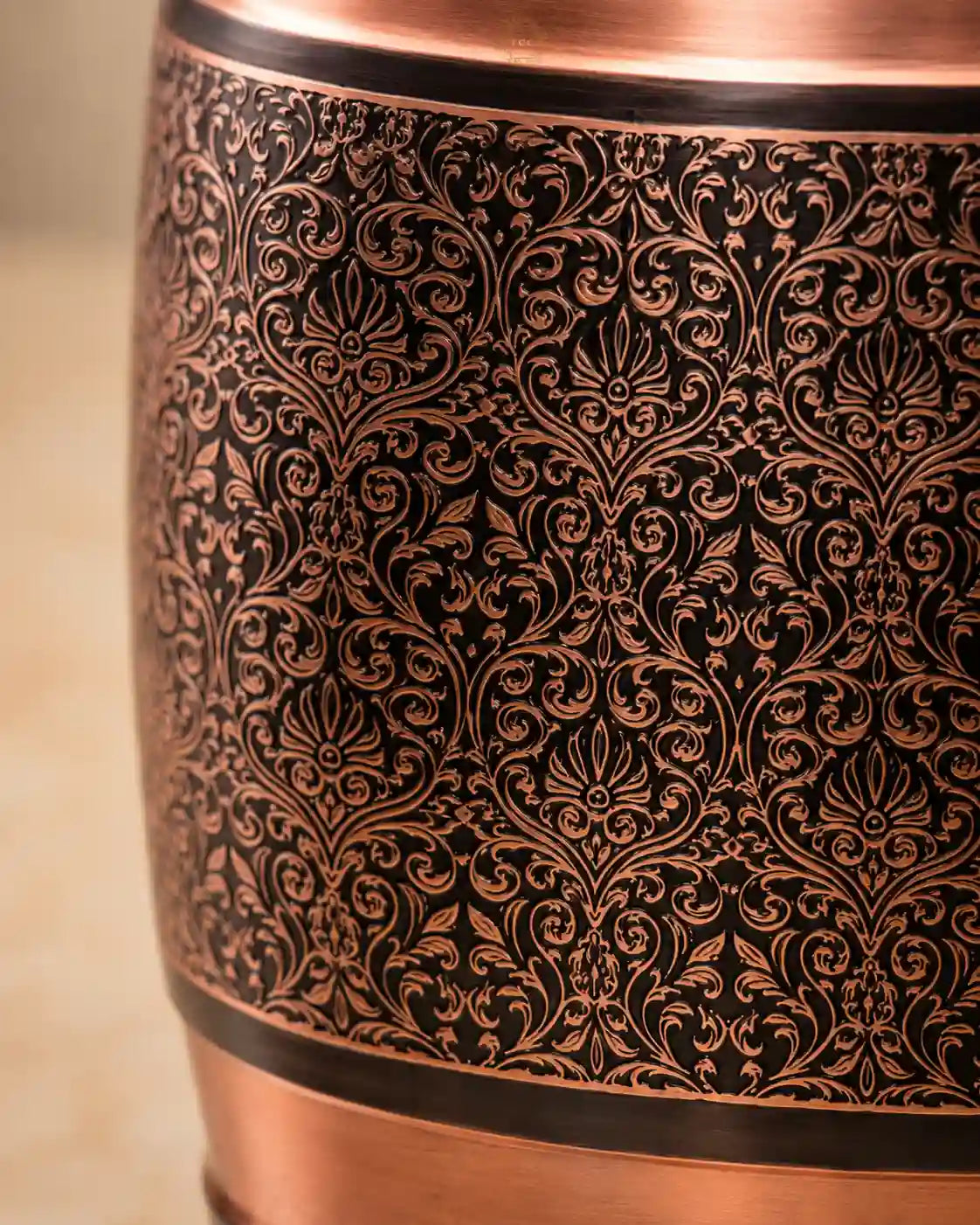 Close-up of a Pure Copper Water Dispenser object featuring an intricate black damask-style filigree pattern, with polished copper bands at the top and bottom.