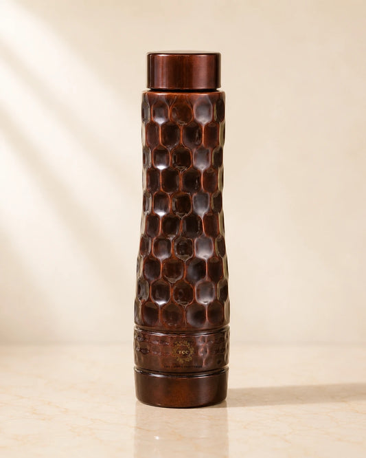 Antique Diamond Copper Water Bottle  with a honeycomb pattern and a matching lid, standing on a light beige marble surface against a warm beige background.