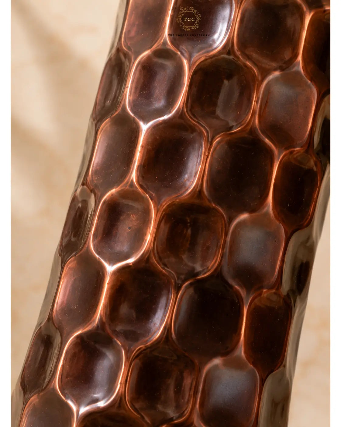 Close-up of a Antique Diamond Copper Water Bottle with a warm copper-brown tone and reflective highlights, set against a softly blurred beige background.
