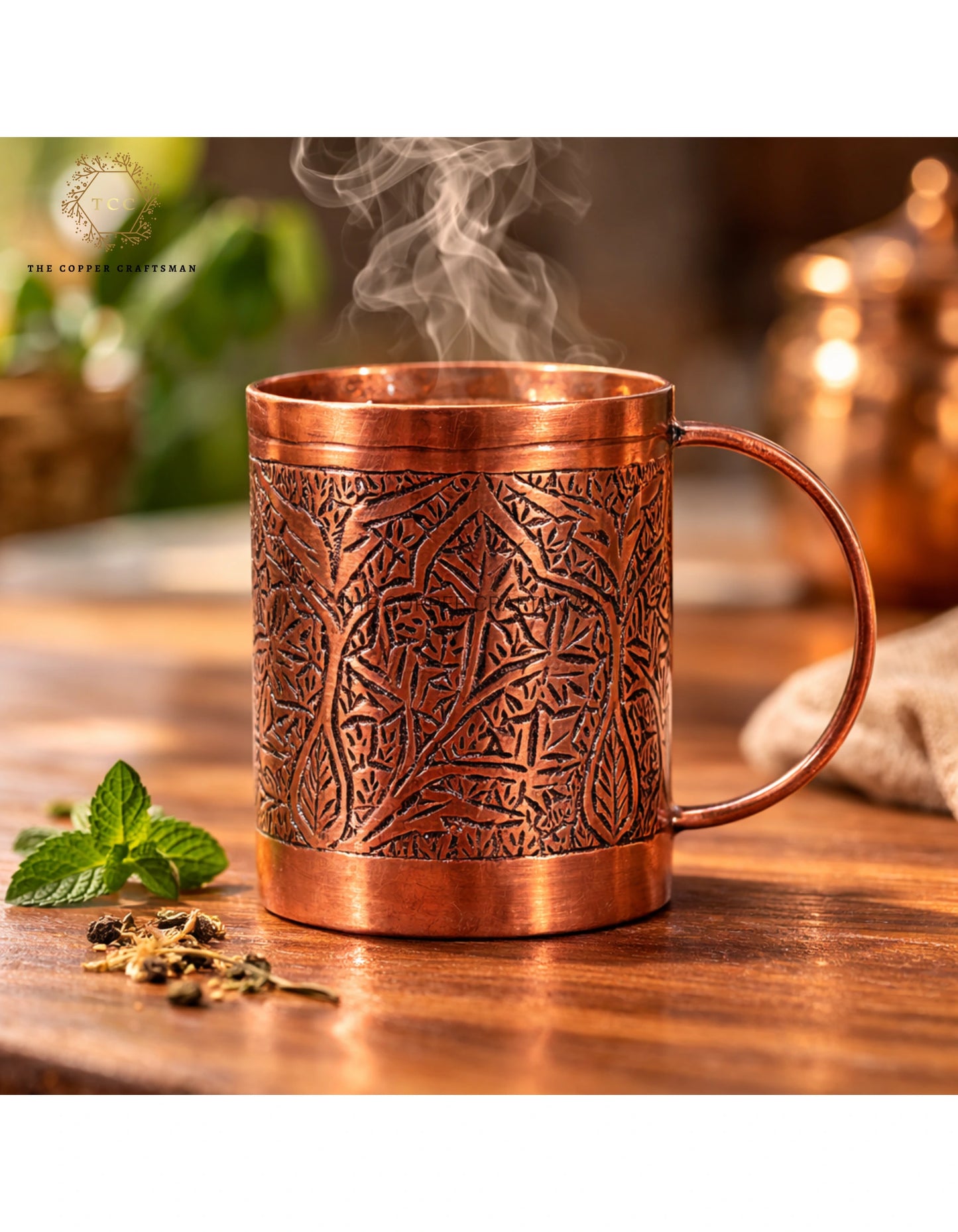 Copper mug with intricate patterns on a wooden surface, surrounded by mint leaves and tea leaves.