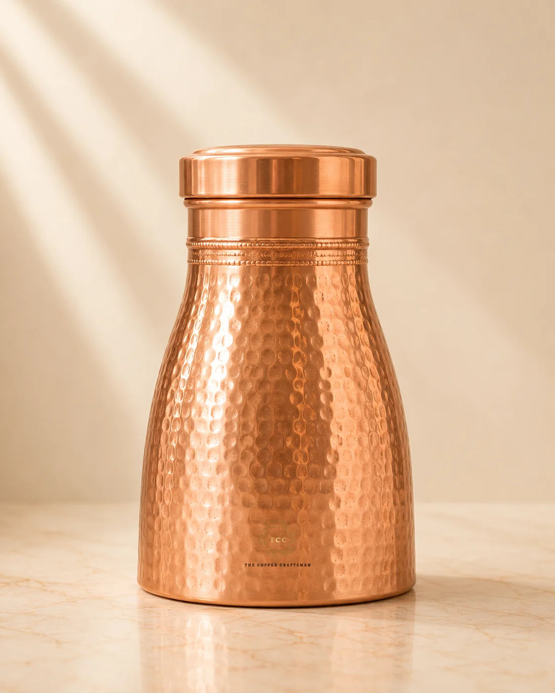 A Copper Bedroom Jar 1Lwith a matching lid, standing on a light marble surface against a warm beige background with soft diagonal shadows.