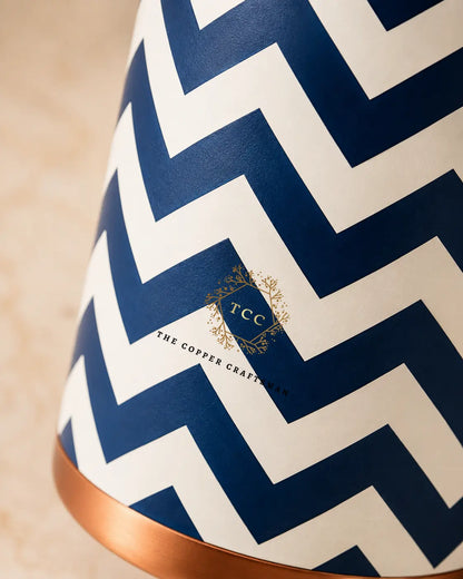 Close-up of a cylindrical copper-bottle with a navy and off-white chevron pattern and a small gold 'TCC The Copper Craftsman Show' logo near the center.