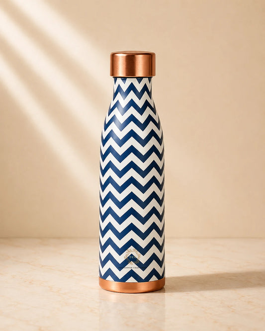 A Copper Water Bottle 1000ml (PRINTED) with a navy and white chevron pattern and a metallic rose gold cap, standing on a light marble surface against a beige background with soft diagonal shadows.