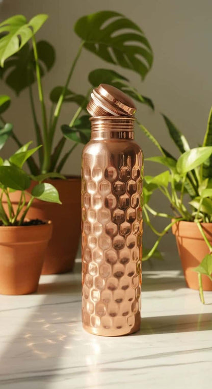 Copper water bottle with textured design on a surface with plants in the background