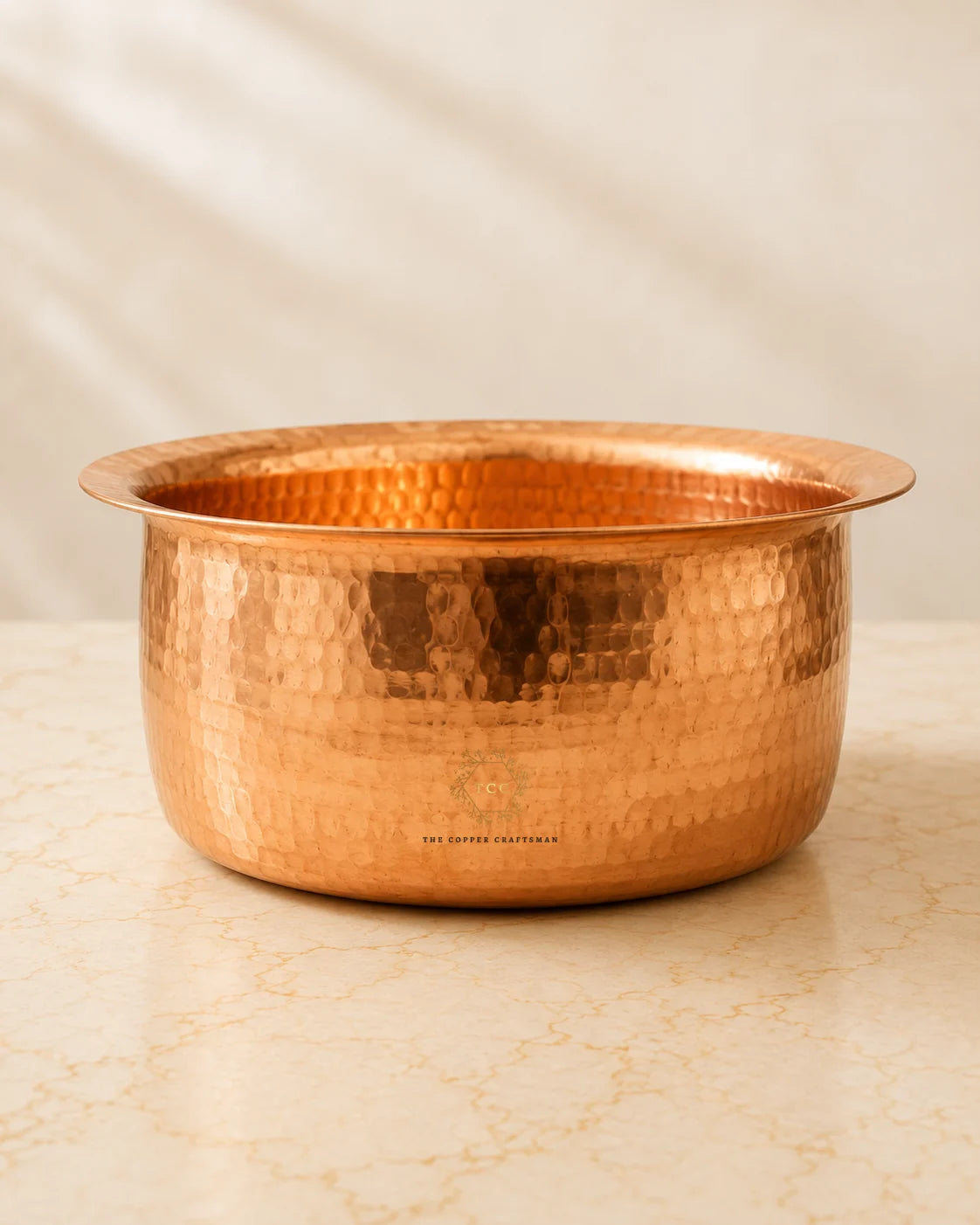 A hammered copper bowl 4.2 L with a flared rim, sitting on a light beige marble surface against a soft beige fabric backdrop.
