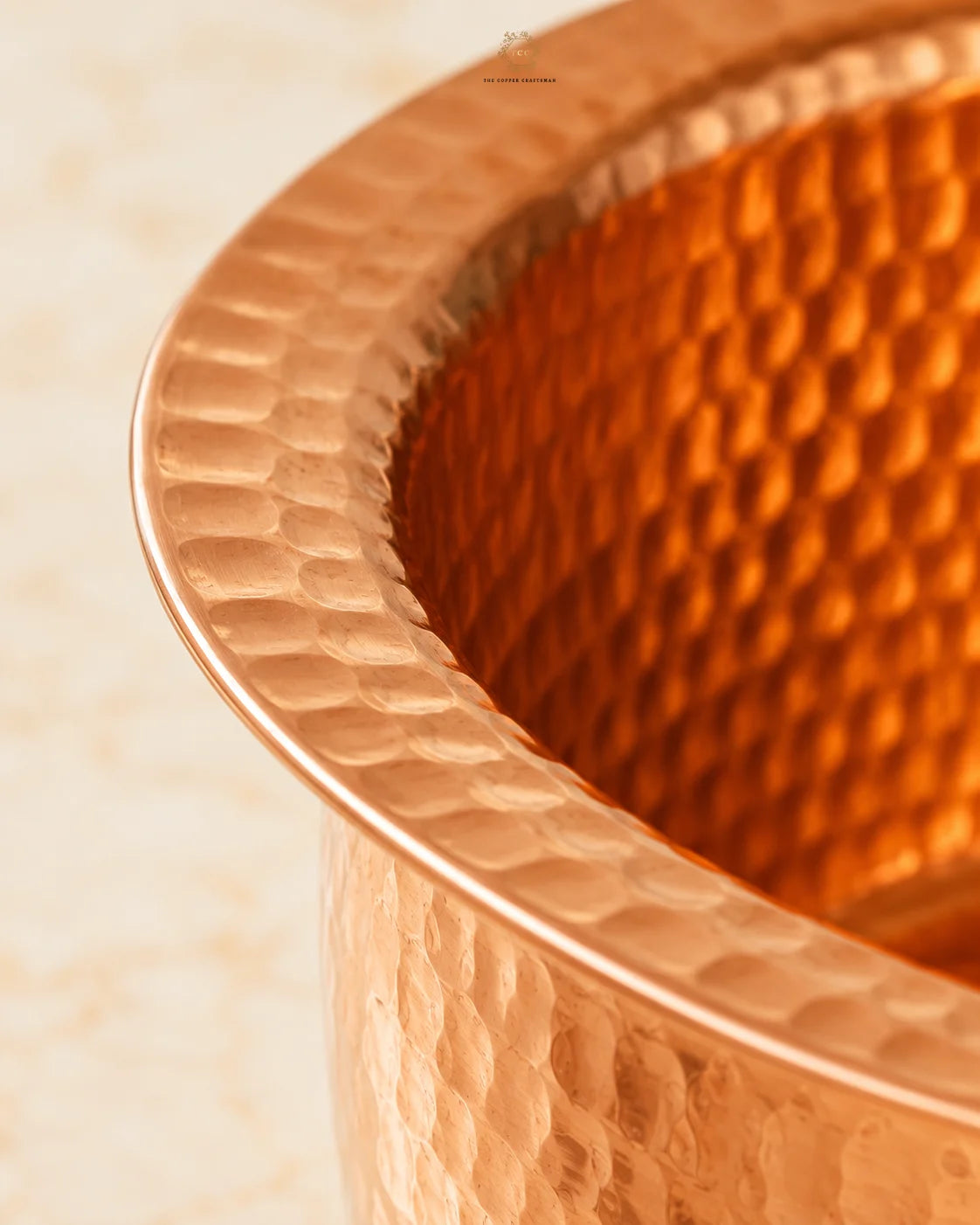 Close-up of a hammered Hammered Copper Cooking Pot (4.2 Litres)showing its textured metallic rim and warm copper interior against a light beige background.