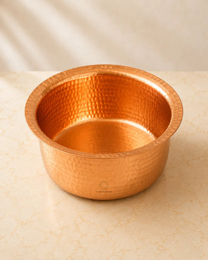 A Hammered Copper Cooking Pot (4.2 Litres)with a wide rim, sitting on a light beige marble surface with a soft beige background.
