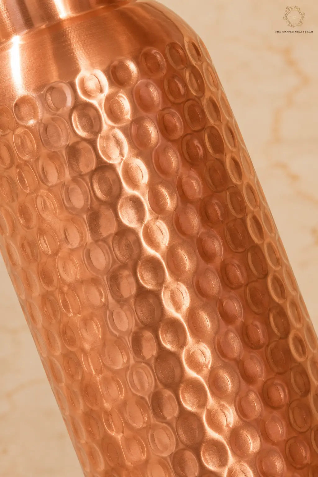 Close-up of a hammered copper water bottle showing its textured metallic surface against a light beige background.