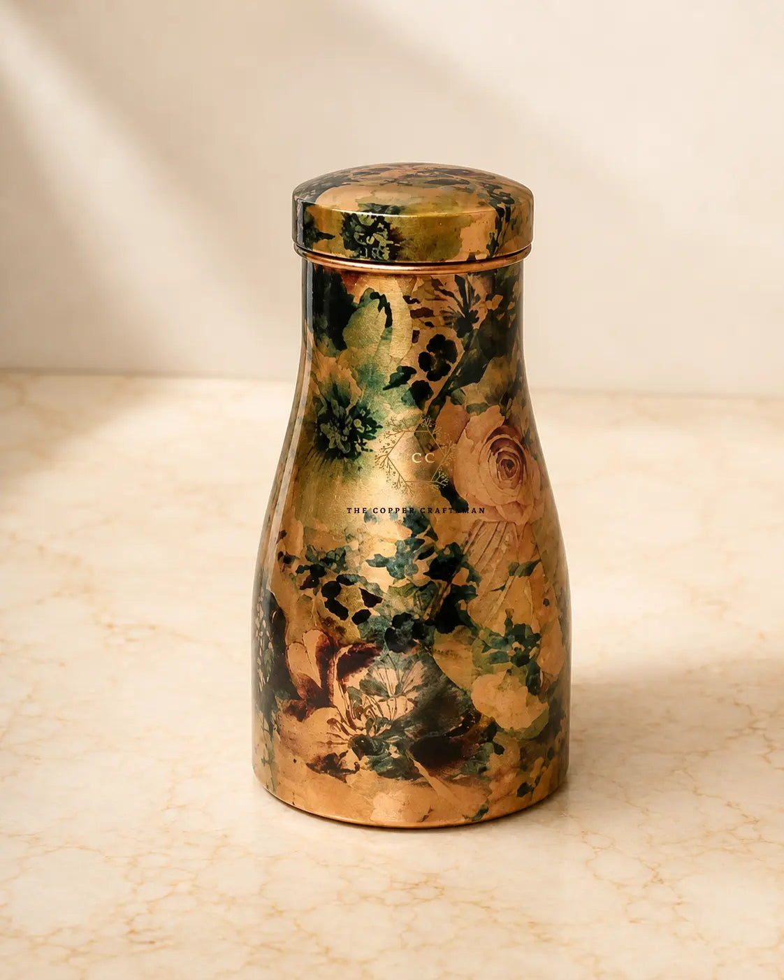 A pure copper water jar 1.5 litre with a matching lid, featuring a vintage floral pattern in gold, green, and beige tones, set on a light marble surface.