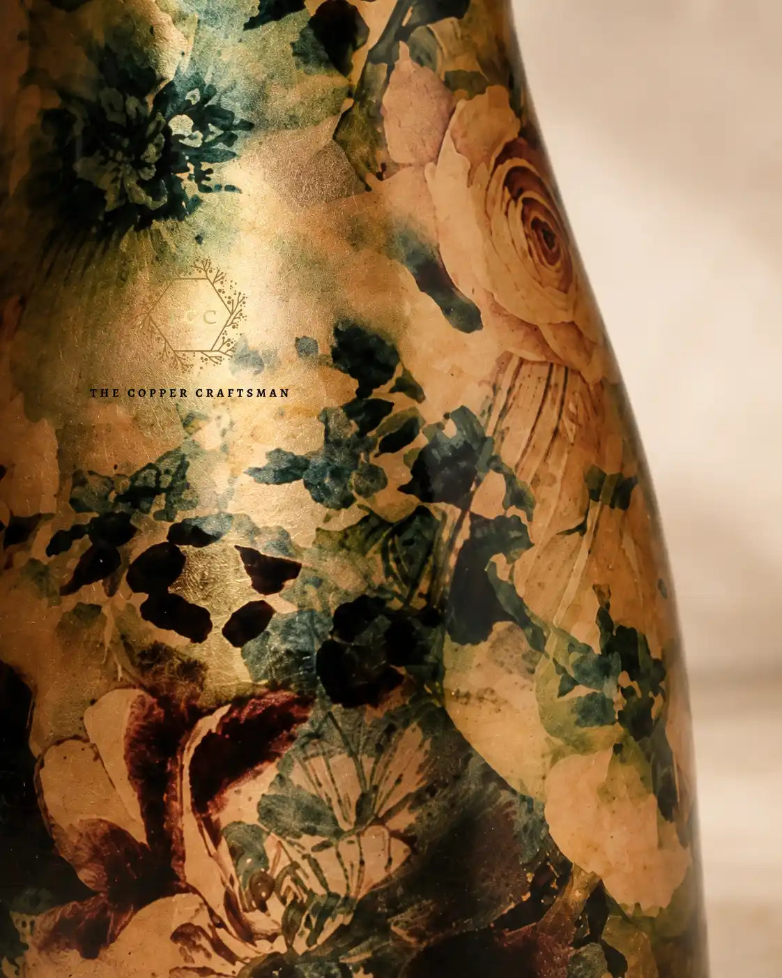 Close-up of a decorative Hand-painted floral pure copper water jar 1.5 litre with an artistic floral print in dark green, black, and warm beige tones. The text 'THE COPPER CRAFTSMAN' is visible on the surface.