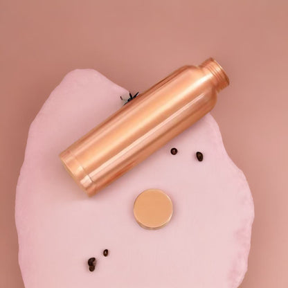 Rose gold water bottle on a pink surface with a brown background
