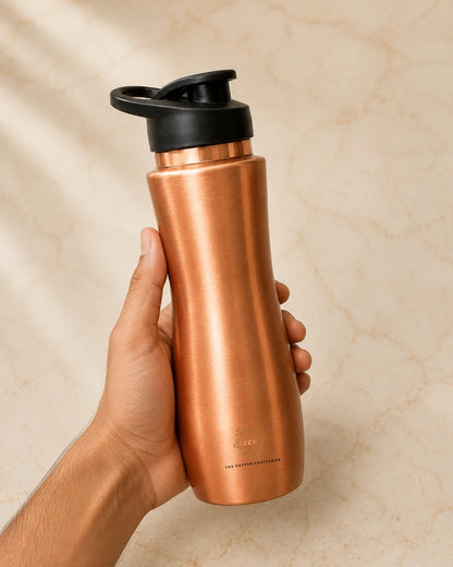 A hand holding a metallic copper water bottle with a black lid against a beige marble background.