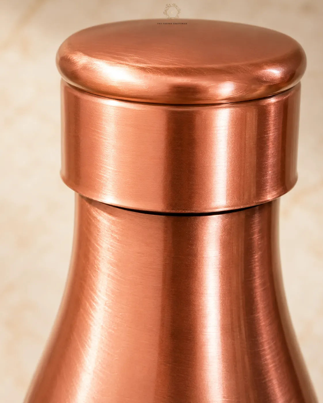 Close-up of a Traditional Pure Copper Water Bottle 1 L with a brushed metallic finish and a matching rounded lid, set against a soft beige background.