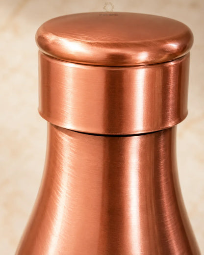 Close-up of a Traditional Pure Copper Water Bottle 1 L with a brushed metallic finish and a matching rounded lid, set against a soft beige background.