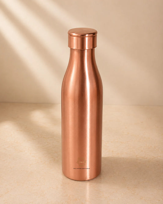 A sleek, Traditional Pure Copper Water Bottle 1 L with a matching screw-on lid, standing on a light beige surface with soft diagonal shadows.