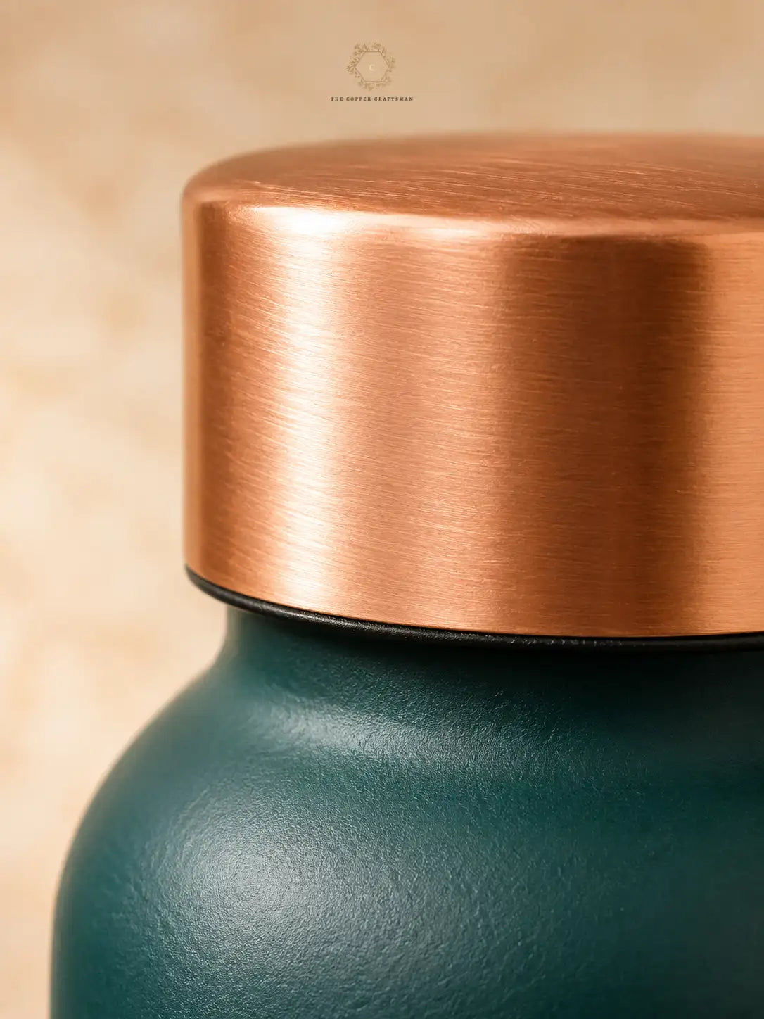 Close-up of a green colour copper water bottlewith a brushed copper lid against a warm beige background.
