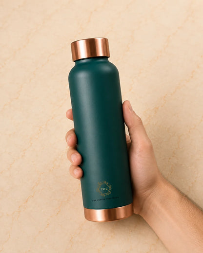 A hand holding a matte green colour copper water bottle with metallic rose gold accents on the lid and base, set against a light beige textured background.