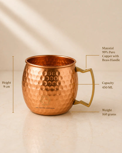 A hammered copper Moscow Mule mug with a brass handle, shown on a warm beige background with measurement callouts indicating height, capacity, weight, and material details.