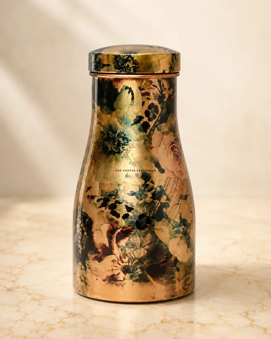 A Hand-painted floral pure copper water jar 1.5 litre with a lid, featuring an artistic floral and botanical print in muted green, brown, and beige tones over a metallic copper base. The brand name 'THE CUPPER COLLECTION' is printed on the front.